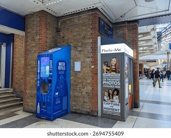 En klassisk fotobox för passfoton placerad intill en blå vattenautomat.