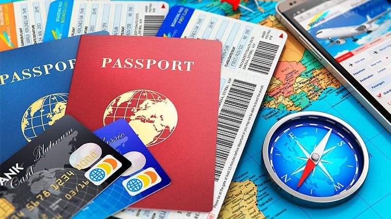 Pass, flygbiljetter, bankkort och en kompass på en världskarta.
