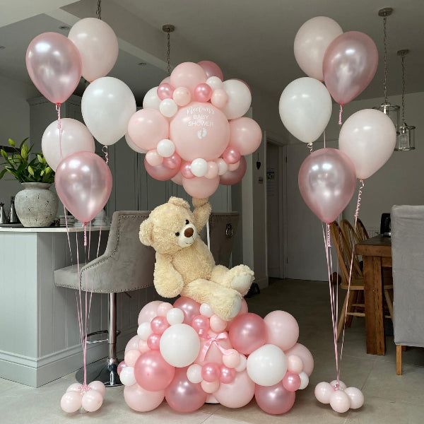 Dekoration till gender reveal med rosa och vita ballonger och en nallebjörn.