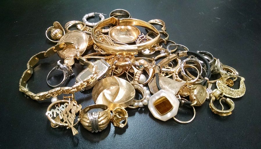 En samling vintage smycken i guld och silver liggandes på en mörk yta.